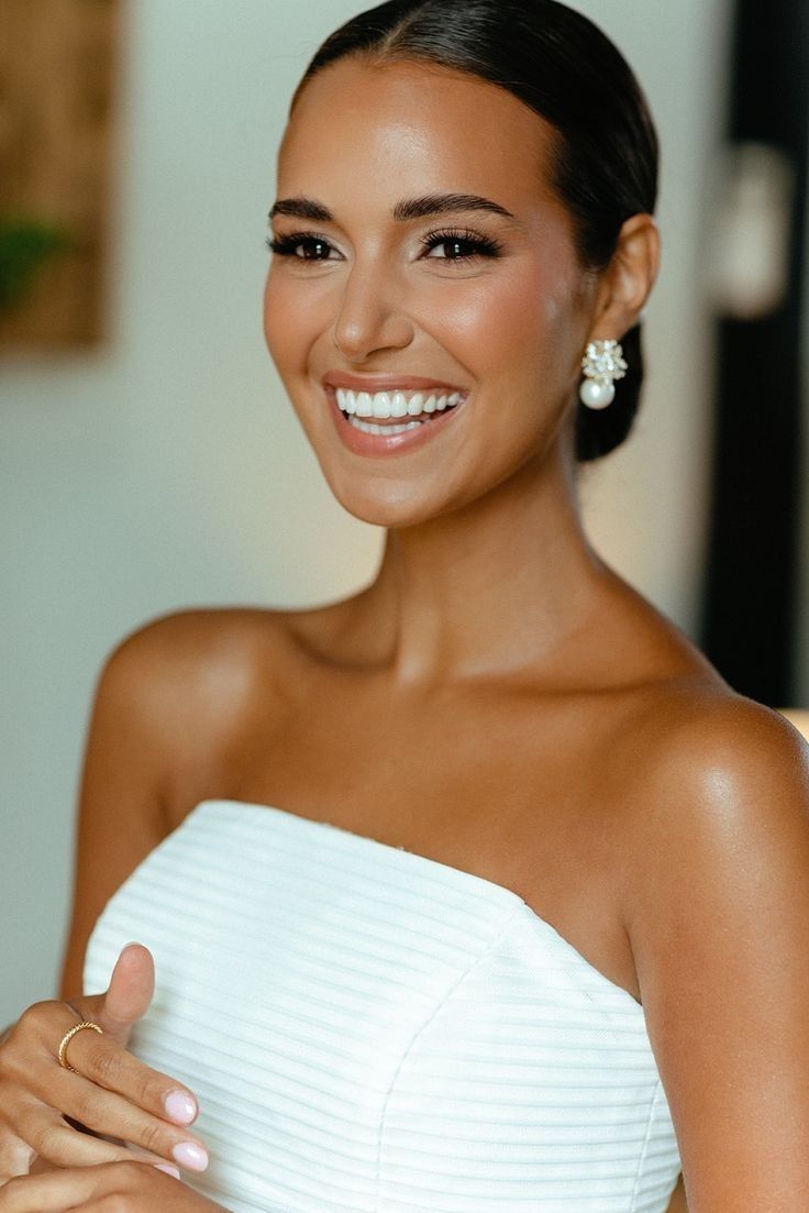 a woman in a white dress smiling and holding her hand on her chest with both hands