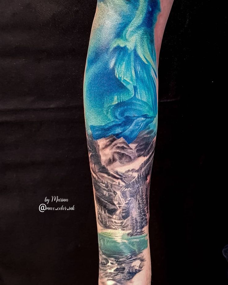 a man's arm with a painting on it that has mountains and water in the background