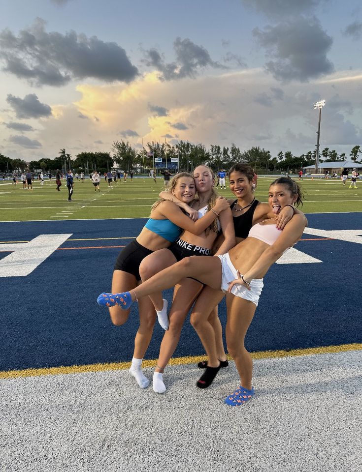 three girls are posing for the camera in front of a football field with their arms around each other