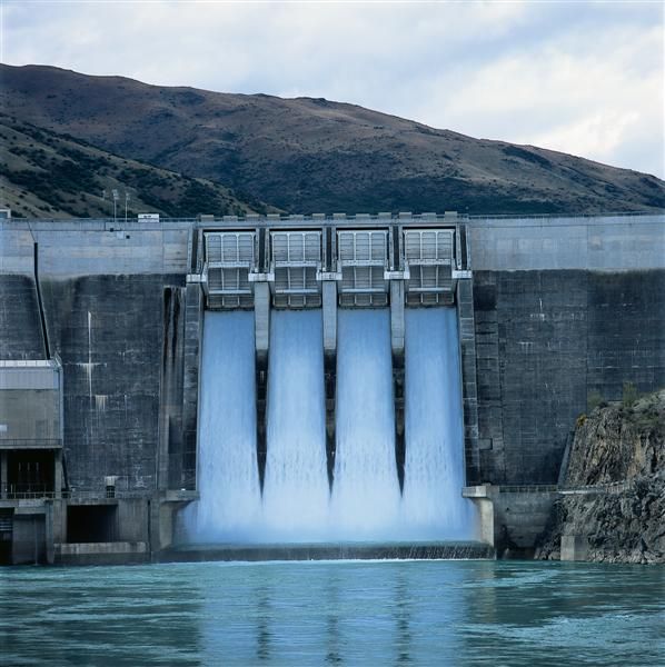 a large dam with water pouring out of it's gates and mountains in the background