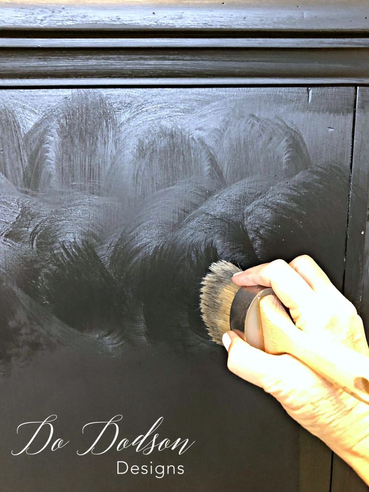 a person is using a brush to paint the side of a black cabinet with white lettering on it