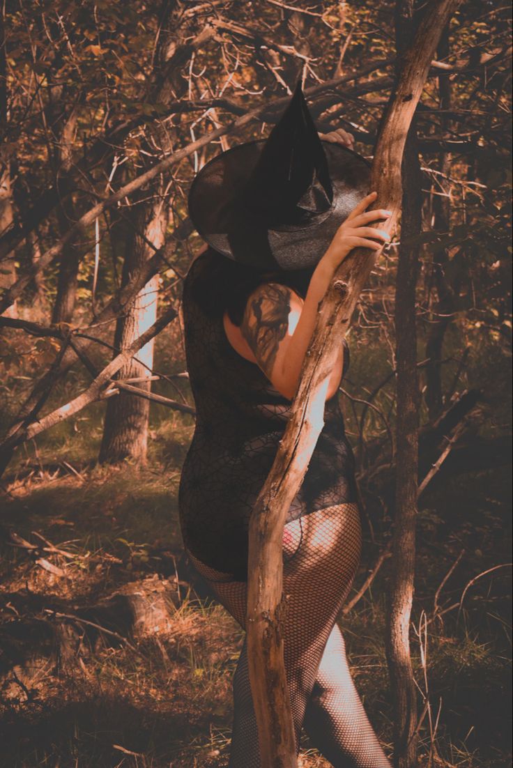 a woman in a black dress and hat leaning on a tree branch with her hands behind her head