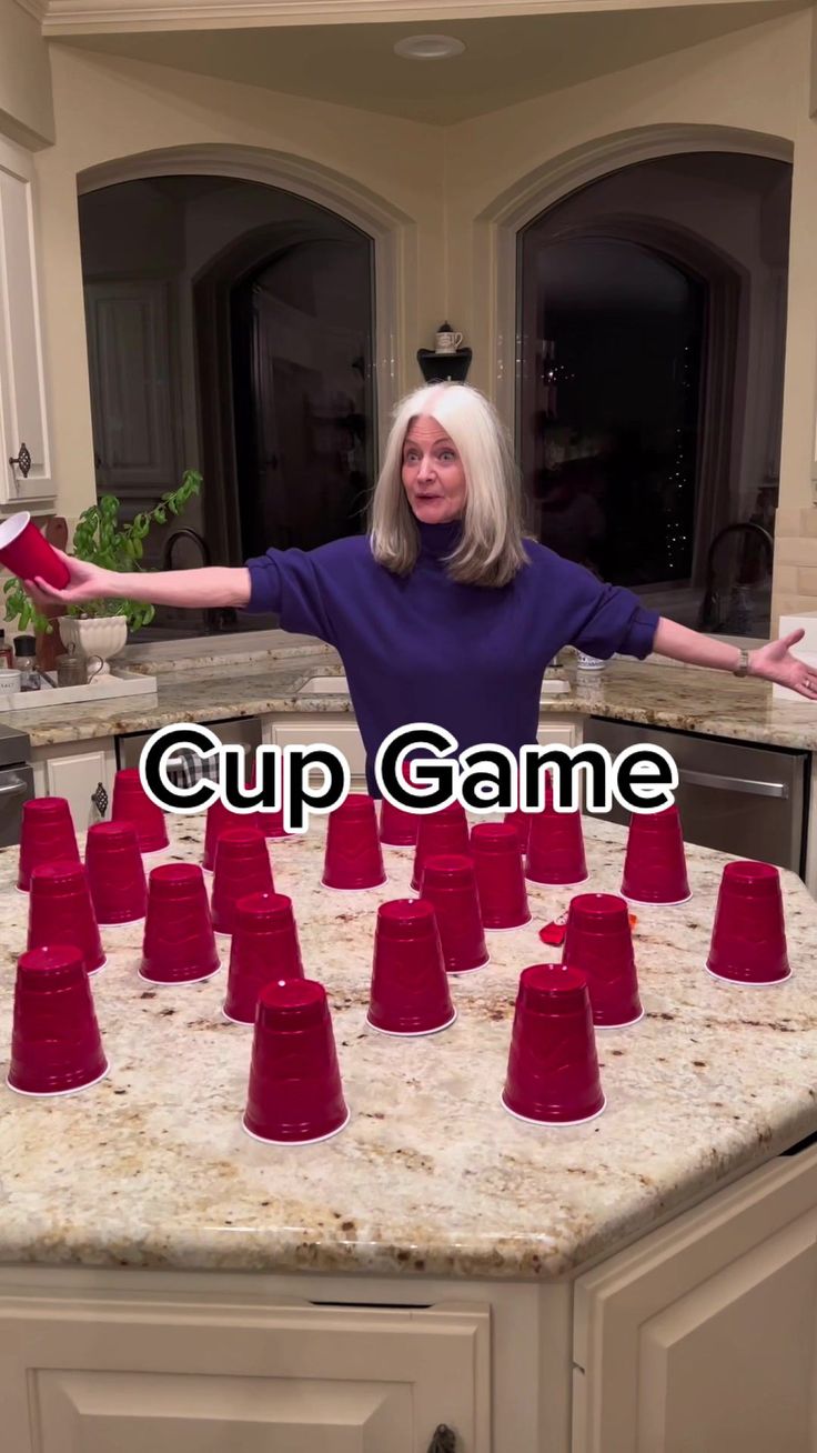 an older woman standing in front of red cups on top of a kitchen counter with her arms outstretched