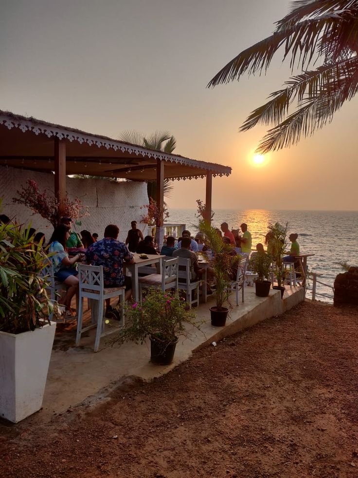 a group of people sitting at tables on the beach with sunset in the back ground