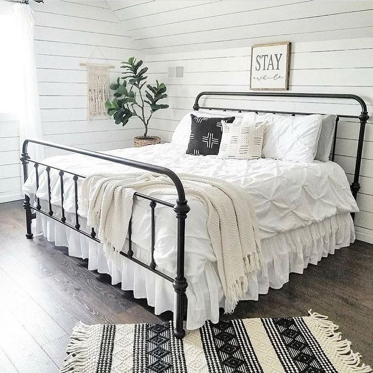 a bedroom with white walls and wood flooring has a metal bed frame that is topped with black and white pillows