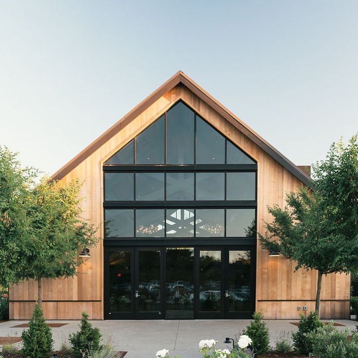 a large wooden building with many windows and trees around it's sides, along with white flowers in the foreground