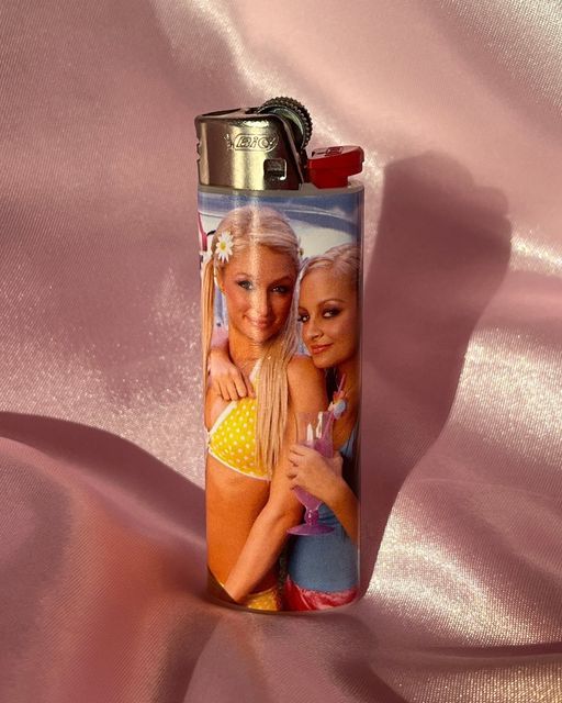 two women are hugging each other on a pink satin background with a lighter in the shape of a can