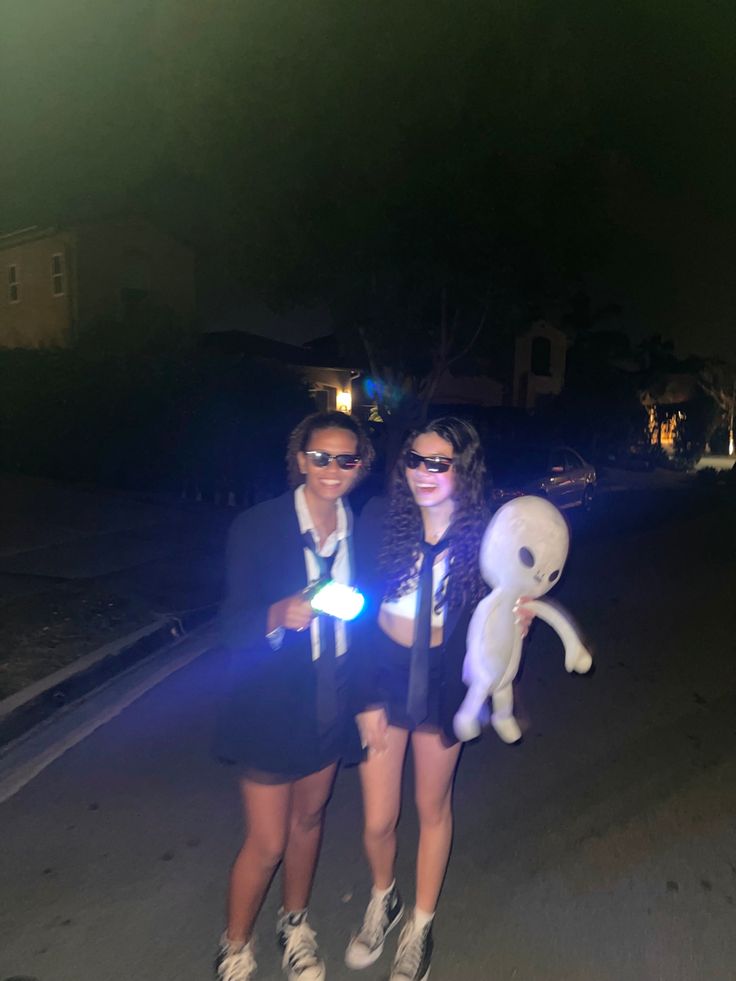 two people standing next to each other in the street at night with their lights on