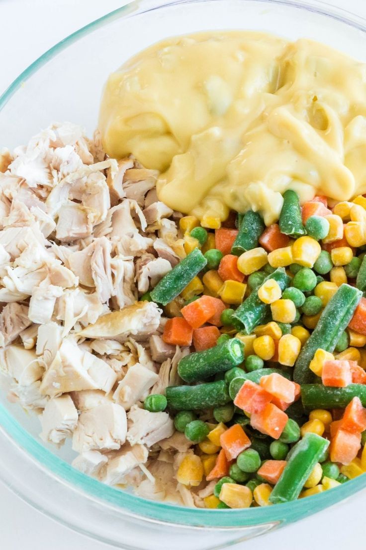 a glass bowl filled with chicken, veggies and mashed potatoes next to a yellow sauce