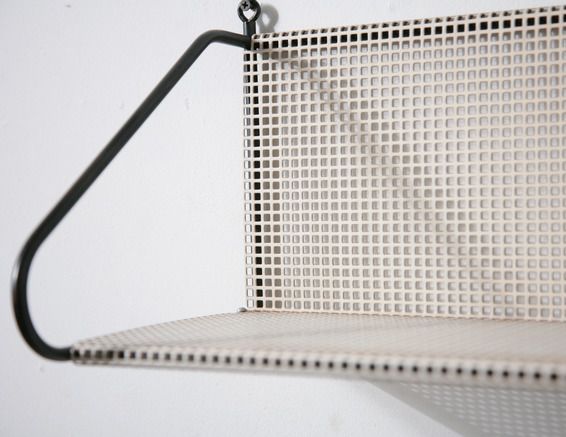 a metal shelf with a black hook on it's side and a white wall in the background