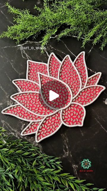 a red and white flower sitting on top of a black table next to green plants