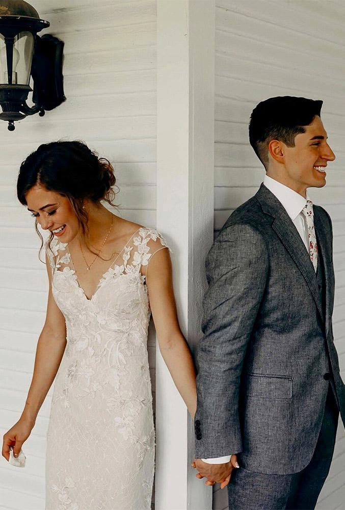 a bride and groom standing next to each other in front of a white wall holding hands