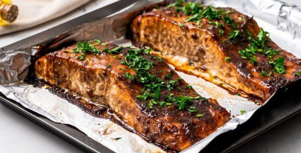 two pieces of meat sitting on top of tin foil covered in sauce and parsley