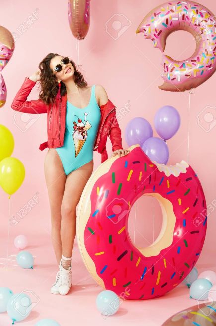 a woman in a bathing suit standing next to a giant doughnut and balloons stock photo