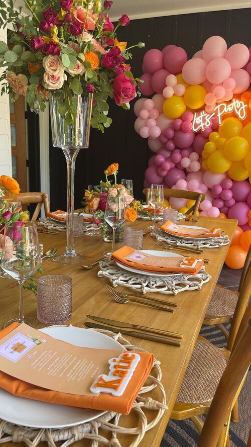 the table is set with plates, napkins and place settings in front of a large balloon wall