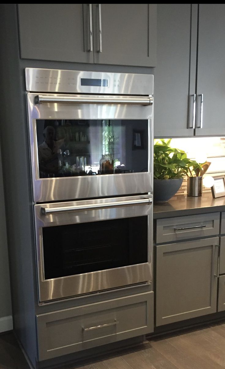 a stainless steel oven in a kitchen with wood flooring and gray cabinets on both sides