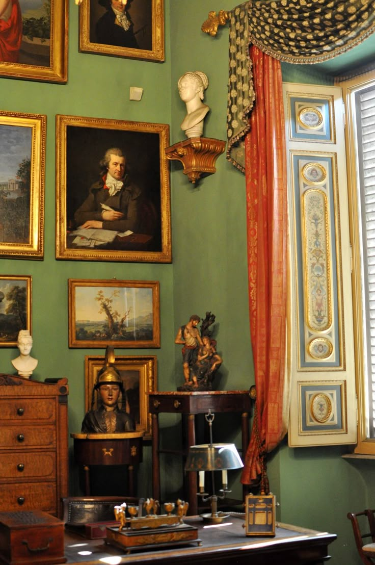 a green room with paintings on the wall and pictures on the walls above it, along with other antique furniture