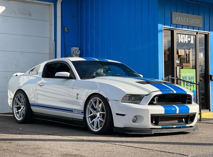 a white and blue mustang parked in front of a building