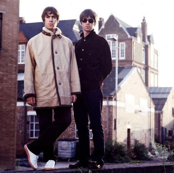 two young men standing next to each other in front of some brick buildings and trees