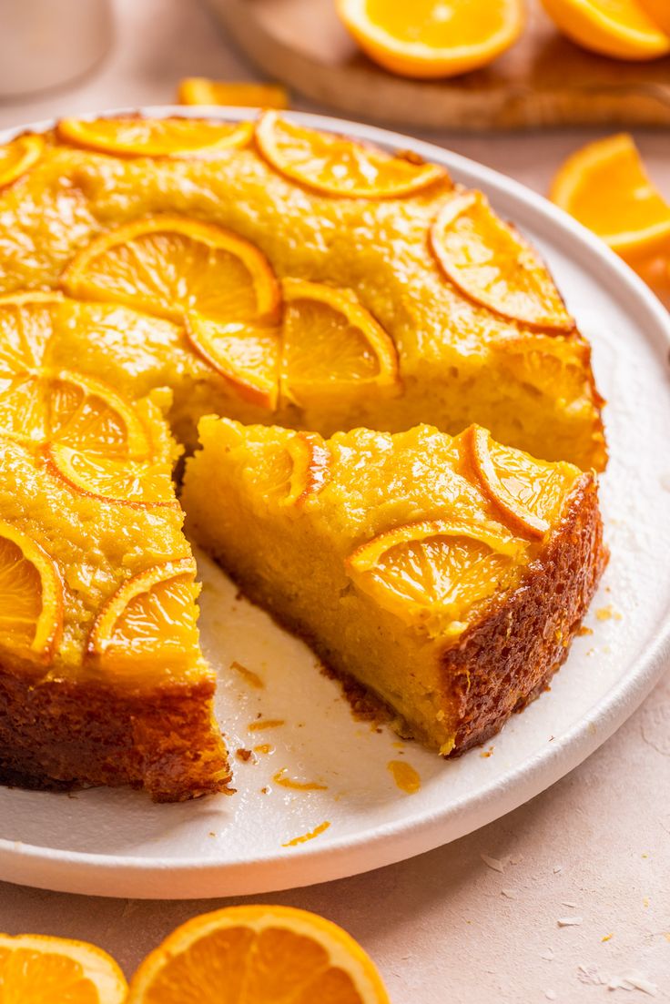 there is a cake that has been cut into slices and placed on a plate with oranges around it