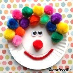 a paper plate with a clown face and pom poms on it's head