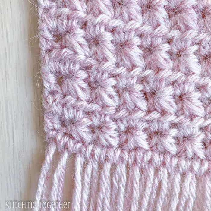 a pink crocheted blanket is laying on a white wooden surface with the end of it