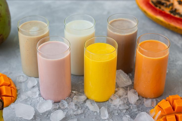 six different types of milkshakes sitting on top of ice with fruit in the background