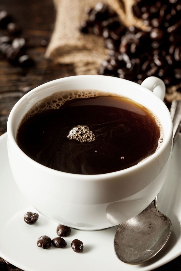 a cup of coffee sitting on top of a white saucer next to some beans