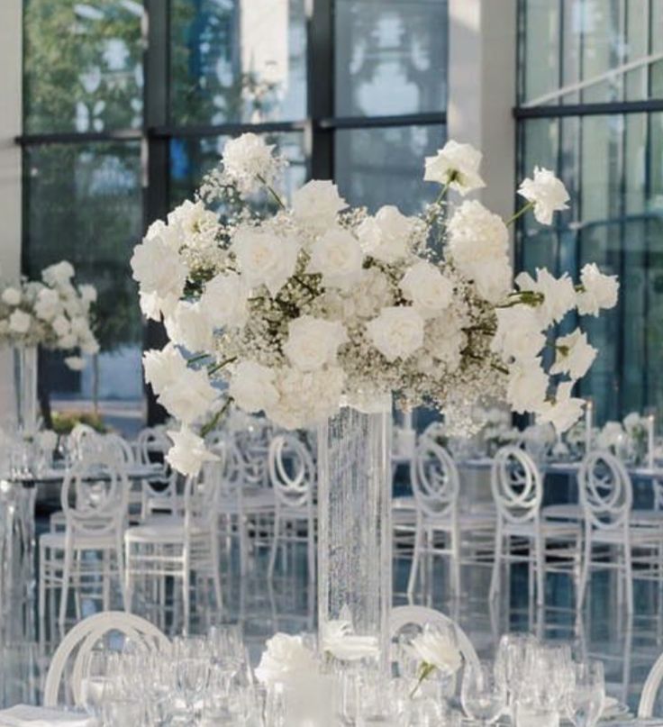 a tall vase filled with white flowers sitting on top of a table covered in chairs