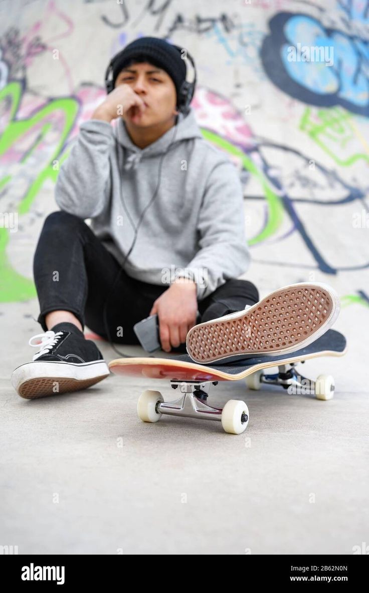 a young man sitting on the ground with his skateboard in front of him - stock image