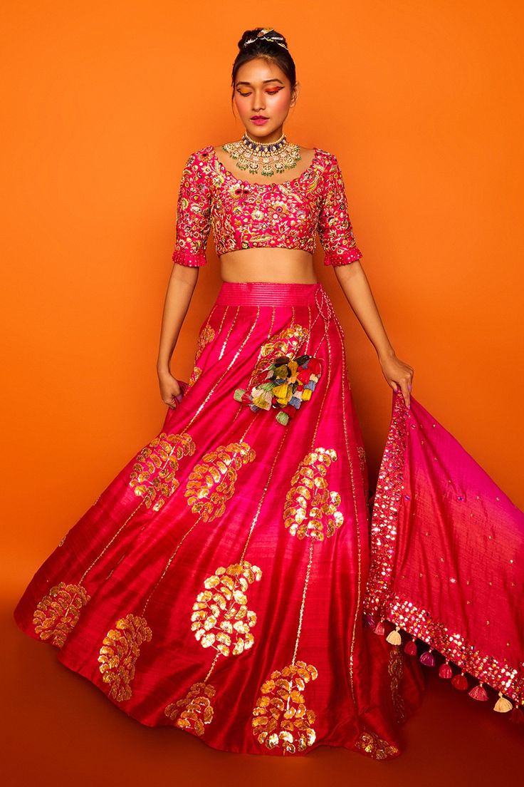 Fuchsia pink lehenga  hand embroidered with clusters of petals in gotapatti and sequined knots forming paisley motifs. Comes with cutwork blouse enhanced with mirrors, gotapatti, sequined knots and  ombre silk dupatta in shades of fuchsia and coral orange.
Components:3
Embroidered
Neckline:Round
Sleeve Length:Half
Fabric:Chanderi silk, raw silk, Tusser Silk
Color:Pink
Tassel dupatta
Pleated sleeve hem
Kamar latkans
Note: Red lehenga set worn by the model to the left is not for sale - Aza Fashion Tassel Dupatta, Cutwork Blouse, Paisley Motifs, Pink Lehenga, Red Lehenga, Pleated Sleeves, Pink Tassel, Embroidered Neckline, Silk Dupatta