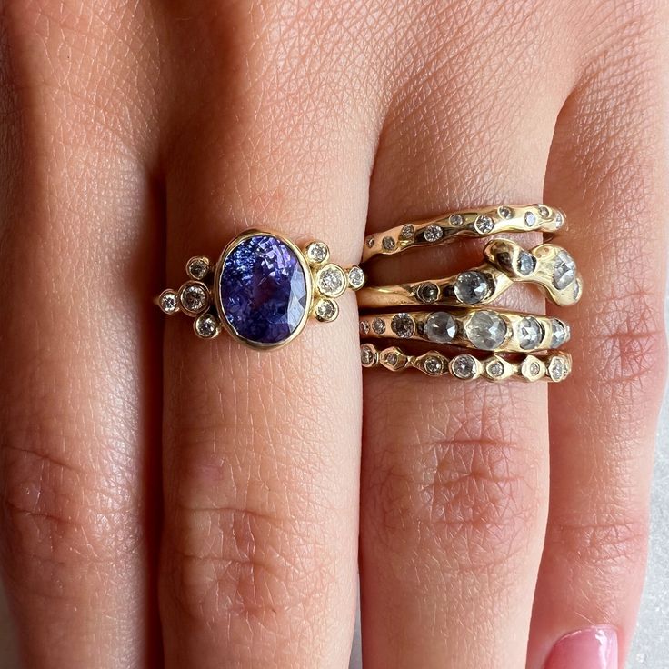 A oval cut Tanzanite is set in 14k yellow gold on a freeform gold band, accented by two 3pt and six 1pt brilliant white diamonds. Approximate stone size: 9mm x 6mm ﻿Handcrafted with love in our Hudson Valley Studio. Please allow 14-21 business days to ship. ACCOMPANYING HALO BAND SOLD SEPARATELY. Unique Oval Diamond Ring With Accents, Oval Stackable Rings With Rose Cut Diamonds For Anniversary, Gold Oval Diamond Ring With Unique Style, 14k Gold Stackable Rings With Accent Stones, Anniversary Stackable Rings With Rose Cut Diamonds, Oval Stackable Rings With Accent Stones, Unique Gold Oval Diamond Ring, Unique Oval Yellow Gold Diamond Ring, Yellow Gold Tanzanite Jewelry With Gemstone Accents