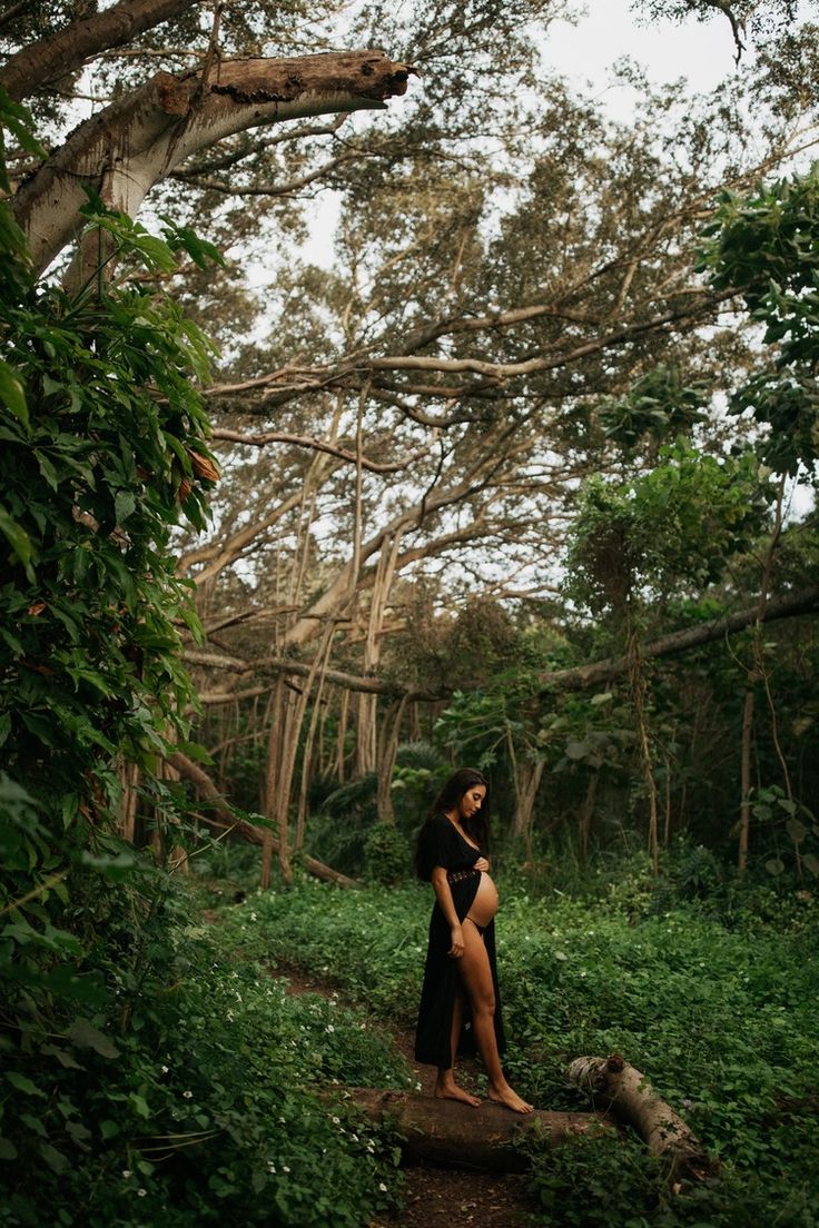 a woman standing in the middle of a lush green forest with trees and bushes around her