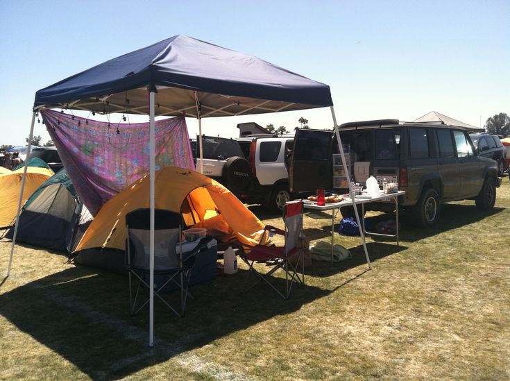 several tents set up on the grass with cars parked in the background and people sitting under them