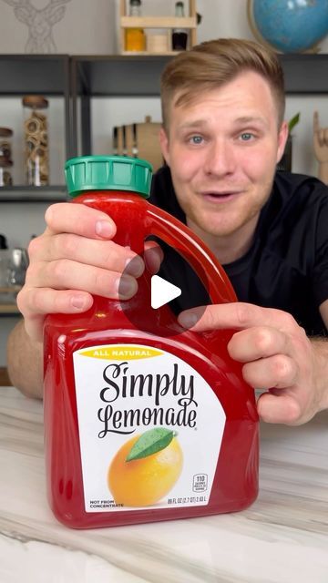 a man holding a bottle of simply lemonade on top of a table in front of him