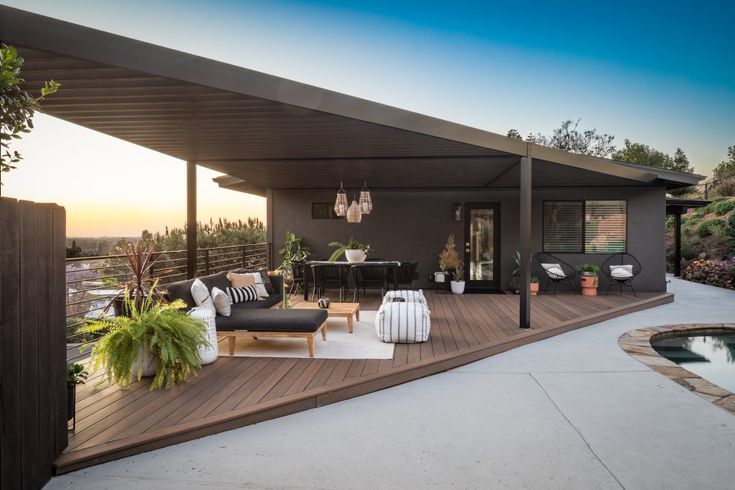 an outdoor living area with wooden decking and patio furniture, overlooking a pool at sunset