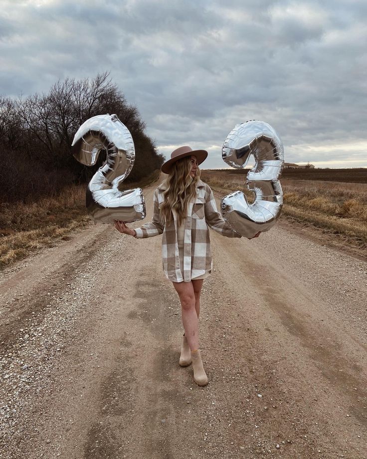 a woman standing in the middle of a dirt road holding up two large letters that spell out 30