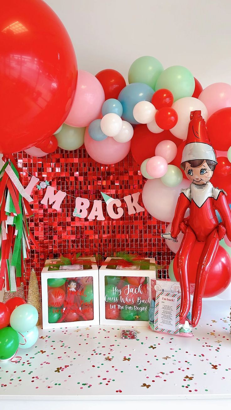 a table with balloons, confetti and an elf figure on it's head