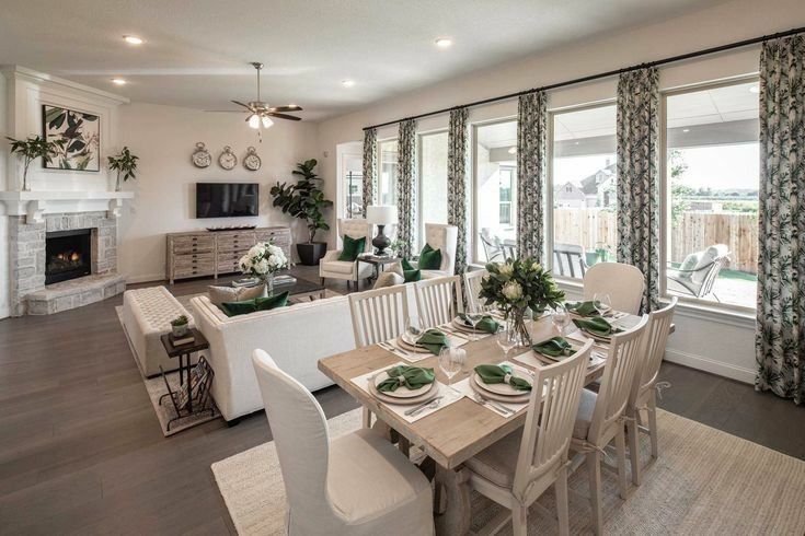 a dining room table and chairs in front of a large window with curtains on it