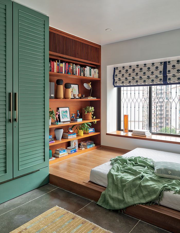 a bedroom with green shutters and bookshelves next to a bed in front of a window