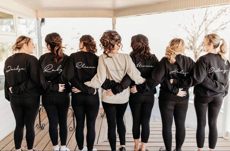 a group of women standing next to each other wearing black sweat suits with white lettering on them