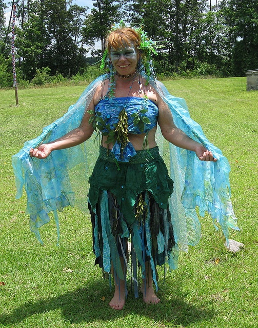 a woman dressed in green and blue is standing on the grass with her arms spread out