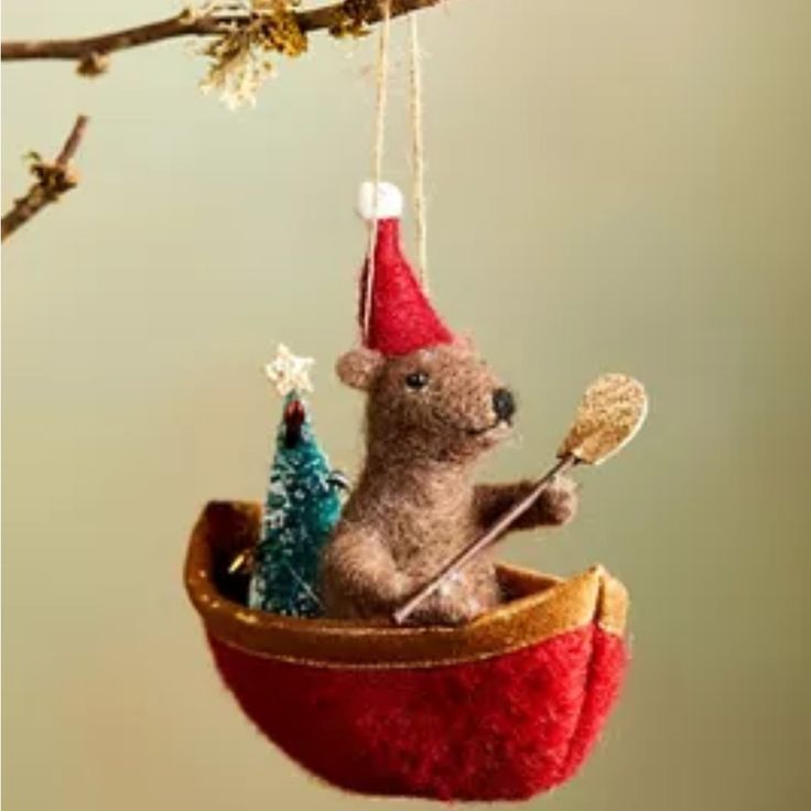 a teddy bear in a boat ornament hanging from a tree branch with christmas decorations