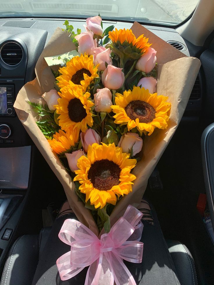 a bouquet of sunflowers sitting in the front seat of a car with a pink ribbon