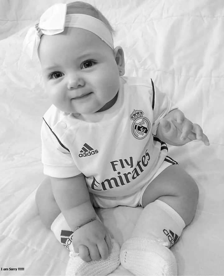 a black and white photo of a baby wearing a soccer jersey smiling at the camera