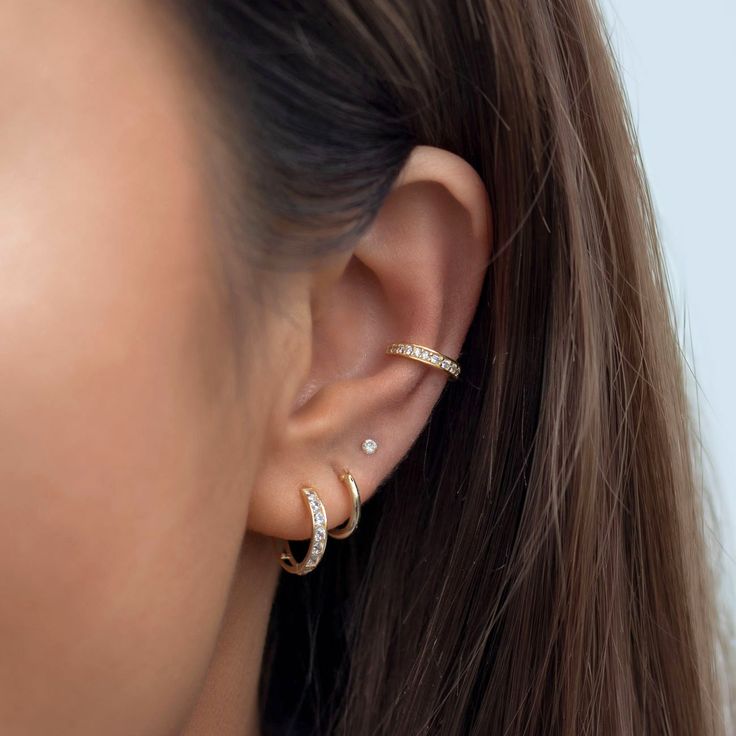 a close up of a woman's ear wearing gold and diamond hoop earrings,