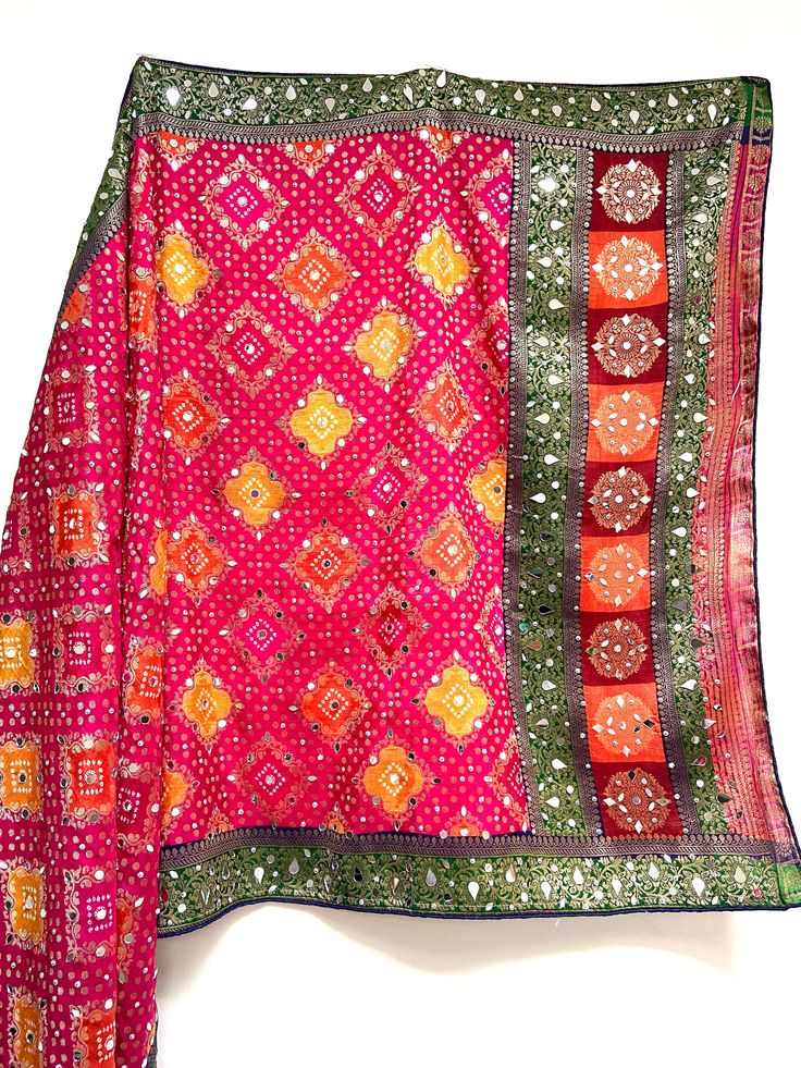 This is an eye catching mirror work silk dupatta with bandhaj work throughout. Bandhaj is a tie dye technique traditionally used in Rajasthan, India, used across multiple items of clothing.  The delicate gold threads are shown in traditional patterns throughout and are perfect for a mendi or pre wedding party to add that colour and sparkle to any simple outfit.  Need a matching suit to go with? Just email info@sagrahi.co.uk for more information.  In stock ready to dispatch and available in other Red Silk Dupatta With Mirror Work, Silk Traditional Wear With Gota Work, Pink Semi-stitched Traditional Wear For Festival, Pink Silk Choli With Mirror Work, Pink Art Silk Saree With Mirror Work, Bohemian Silk Salwar Kameez With Mirror Work, Pink Chinon Salwar Kameez For Traditional Ceremonies, Bohemian Silk Choli With Bandhani Print, Pink Semi-stitched Bohemian Saree