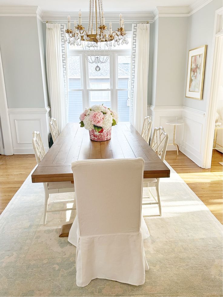 a dining room table with white chairs and flowers in a vase on the centerpiece