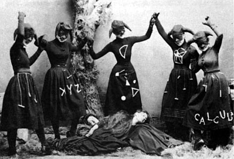 four women with painted faces are standing next to a tree and one is laying on the ground