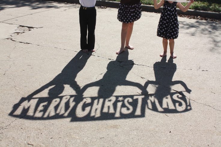 three people standing in front of a sign that says merry christmas with the shadow of two women